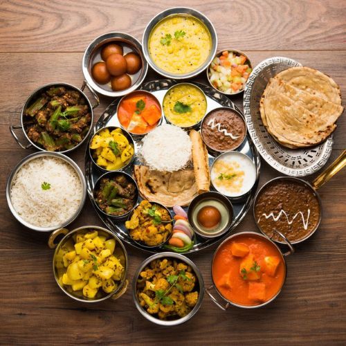 An overhead spread of Indian vegetarian dishes in steel bowls — curries, dal, rice, breads and sweets